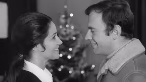 A man and woman smile at each other beneath softly glowing lights