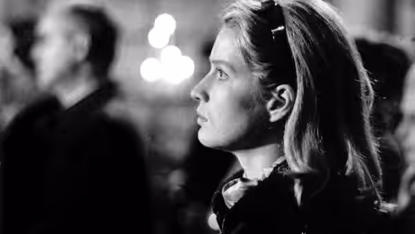 A woman watches from the side as a man sits in the background