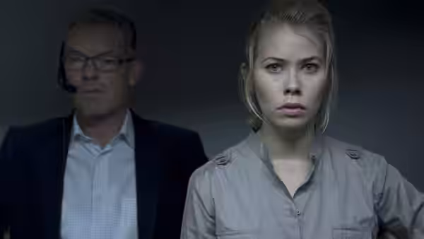 Katrine Fønsmark (Birgitte Hjort Sørensen) stands beside a headset-wearing man