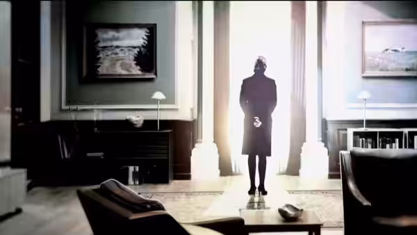 A silhouetted figure stands in a sunlit grand doorway