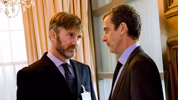 Two men in suits facing each other in formal room setting