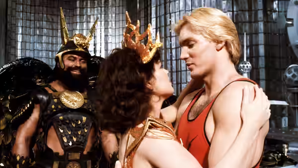 Princess Aura embraces Flash Gordon as Prince Vultan watches from behind