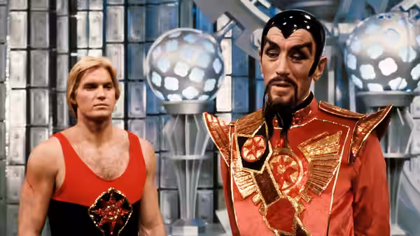 Flash Gordon (Sam J. Jones) stands beside Emperor Ming (Max von Sydow) in a futuristic chamber