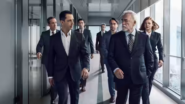 Logan Roy (Brian Cox) and Kendall Roy (Jeremy Strong) walking ahead of a group in an office corridor