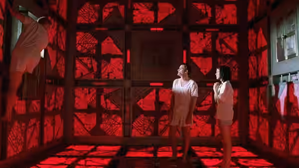 man climbing wall while two others watch in red-lit cube