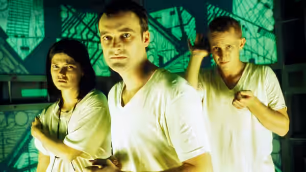 woman with crossed arms beside two men in green-lit room