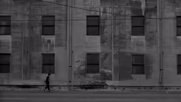 a man walking along a street past a large brick building