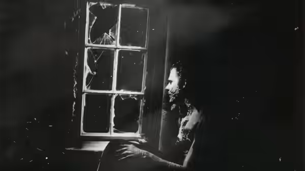 a bearded man sitting by a broken window at night