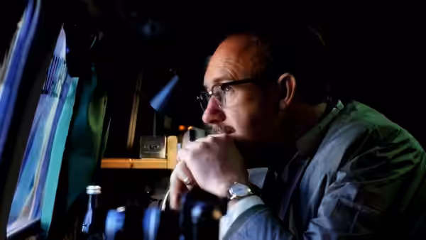 Harry Caul (Gene Hackman) watching a screen while resting his chin on his hand