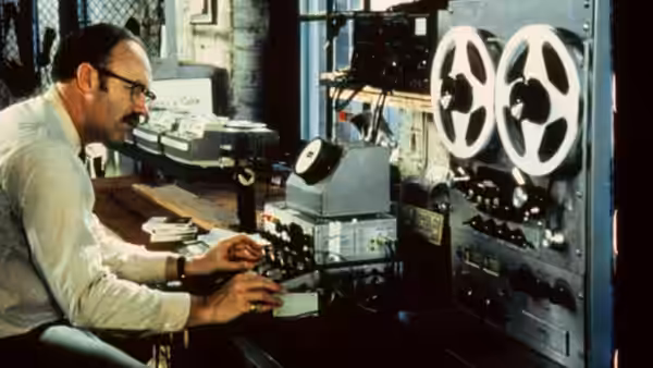 A technician operating reel-to-reel tape machines at a cluttered workbench