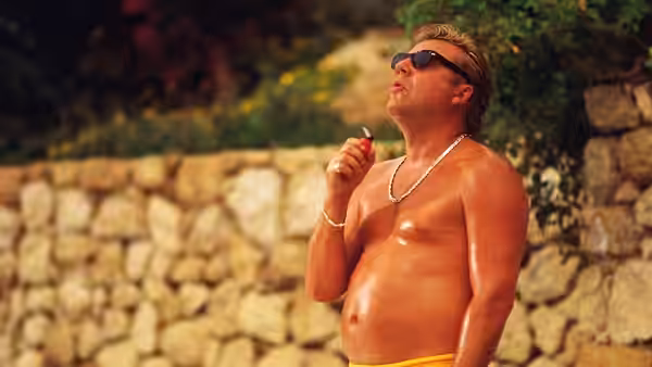 Gal (Ray Winstone) smoking a cigarette outdoors beside a stone wall