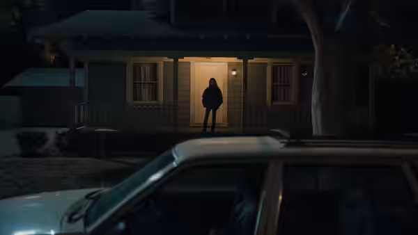 A person in a hoodie stands in the doorway of a house at night