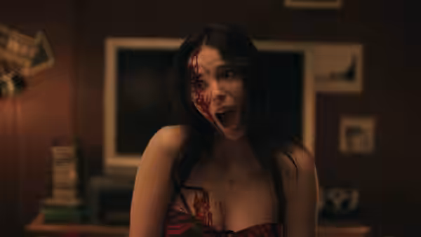 Nikki (Inde Navarrette) with blood on her face stands indoors