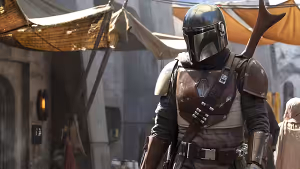 The Mandalorian (Pedro Pascal) stands in a settlement street with fabric awnings overhead