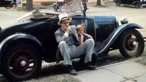 Moses Pray (Ryan O'Neal) and Addie Loggins (Tatum O'Neal) sit beside their car on a roadside curb