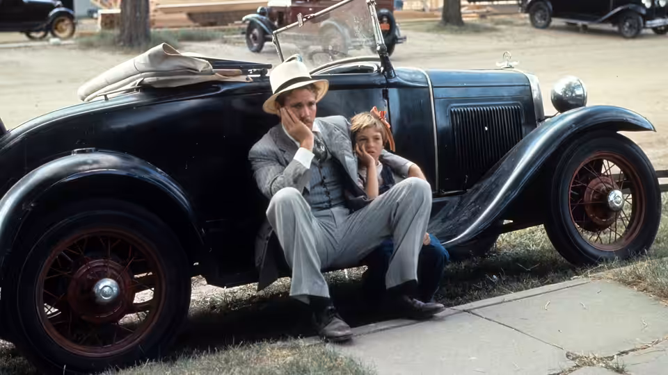 Moses Pray (Ryan O'Neal) and Addie Loggins (Tatum O'Neal) sit beside their car on a roadside curb