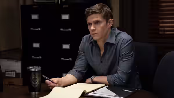 Colin Zabel (Evan Peters) sits at a desk holding a pen in an office