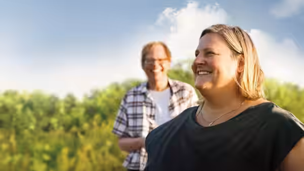 A smiling woman and a man standing together in a sunny field