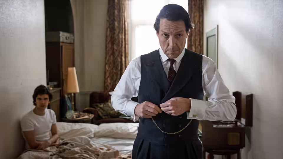 Jeremy Thorpe (Hugh Grant) adjusting his pocket watch chain in a bedroom