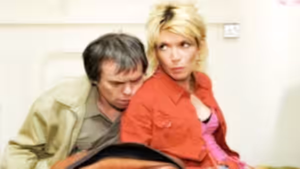 Jill Tyrrell (Julia Davis) and a man look down while sitting closely