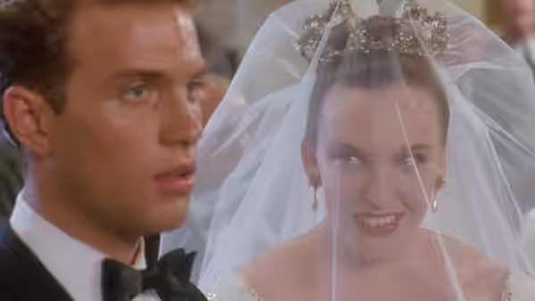 Muriel (Toni Collette) as bride in veil beside a man in tuxedo
