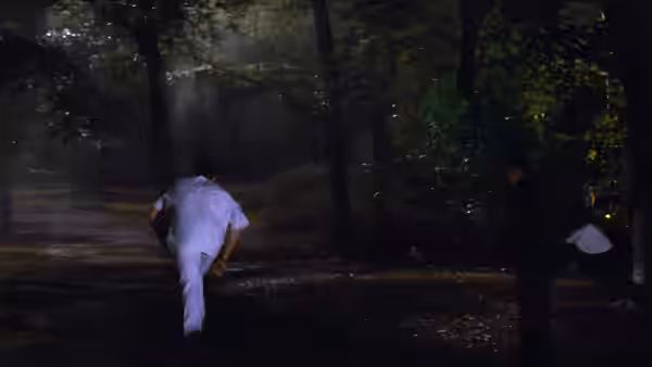 A figure in white clothing runs along a path through dark woods