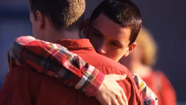 Two young men share a close embrace with one head on a shoulder