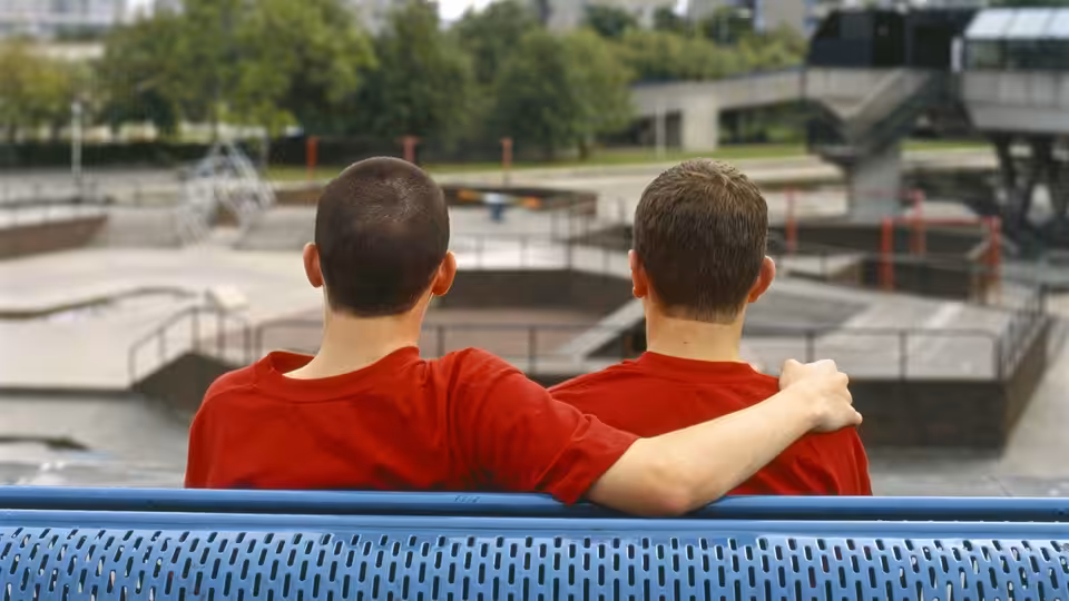 Two teenage boys in red shirts sit side by side on a bench