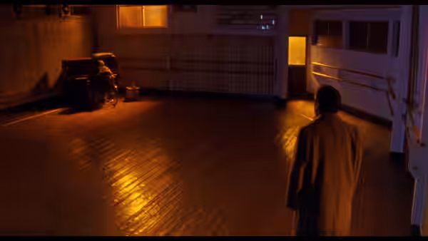 A man in a long coat crosses a wooden-floored room toward a seated figure
