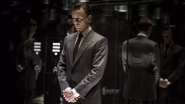 Dr. Robert Laing (Tom Hiddleston) stands with clasped hands in a mirrored elevator