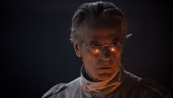 Anthony Royal (Jeremy Irons) looks downward in glasses and a white high-collared outfit