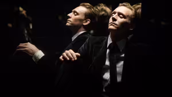 Dr. Robert Laing (Tom Hiddleston) sits beneath his reflection in a dark mirrored room
