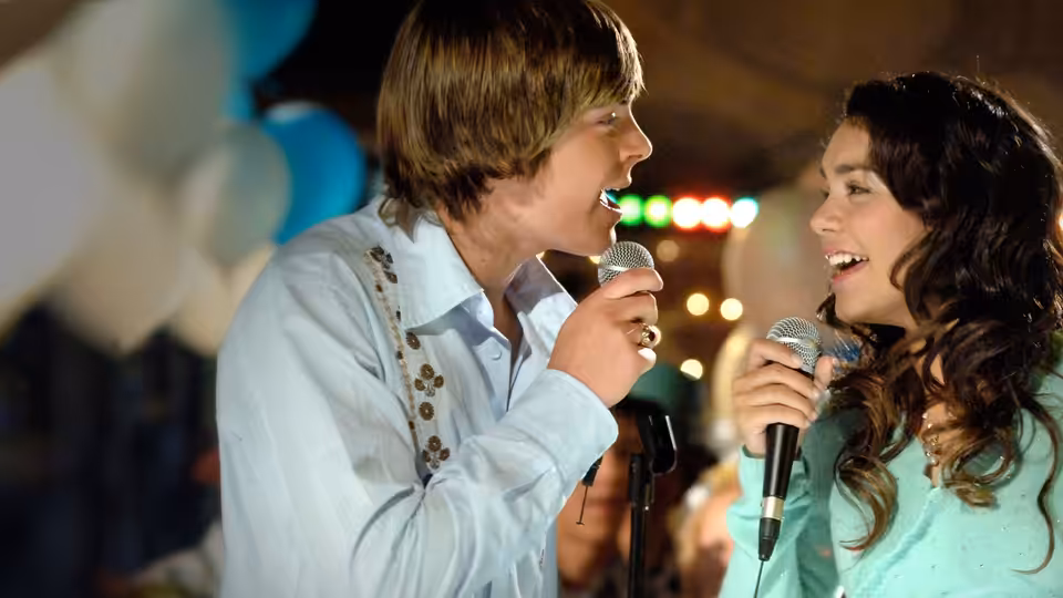 Troy (Zac Efron) and Gabriella (Vanessa Hudgens) singing into microphones on stage