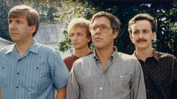 Four men stand together outdoors, looking off in the same direction