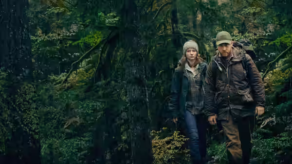 Tom (Thomasin McKenzie) and Will (Ben Foster) walking side by side through dense forest