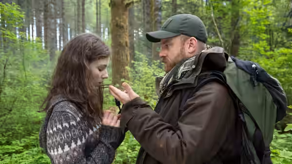 Tom (Thomasin McKenzie) and Will (Ben Foster) examining a small object in the woods