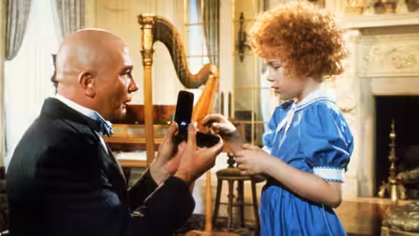 Daddy Warbucks (Albert Finney) shows a small box to Annie (Aileen Quinn) in a study
