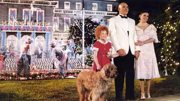 Daddy Warbucks (Albert Finney), Annie (Aileen Quinn) and Grace Farrell (Ann Reinking) stand with their dog