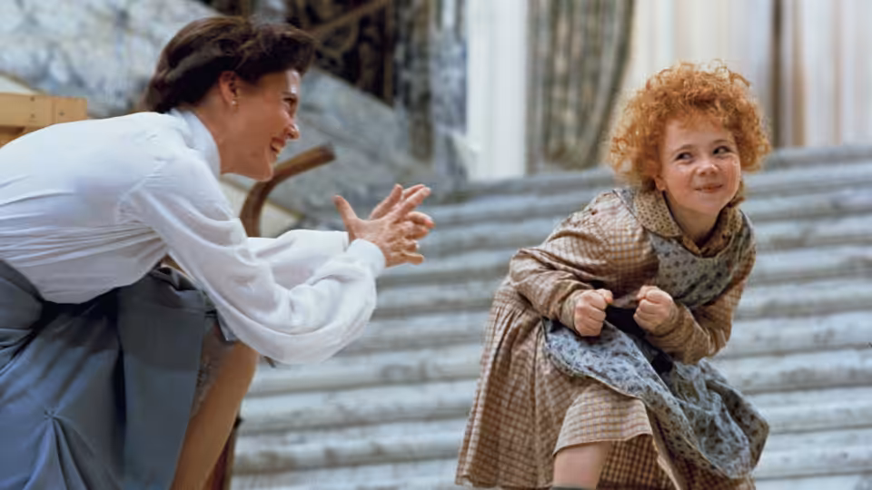 Grace Farrell (Ann Reinking) reaches toward Annie (Aileen Quinn) on wide stone steps