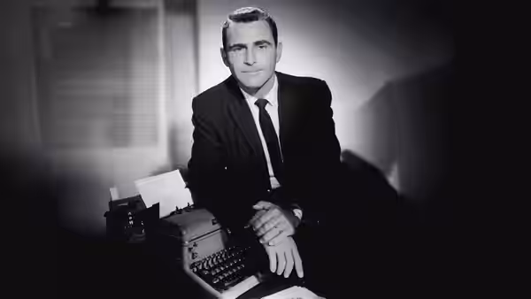 Rod Serling seated at a desk with a typewriter and papers