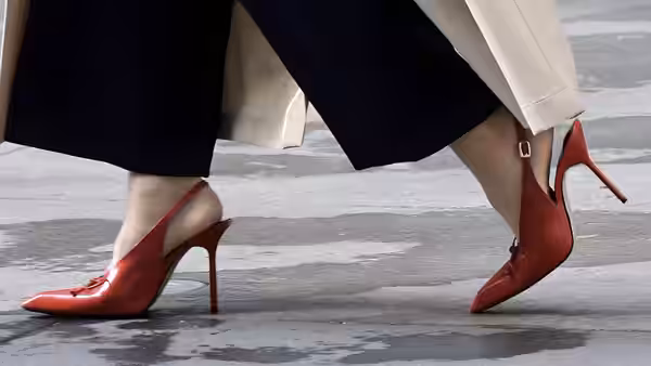 Two pairs of feet in red high heels stepping on wet pavement