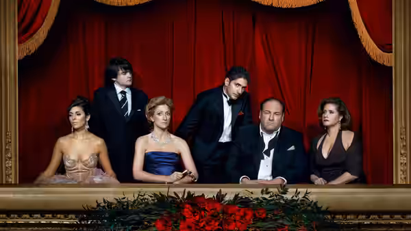 Tony Soprano (James Gandolfini) sits with formally dressed guests before a red theater curtain