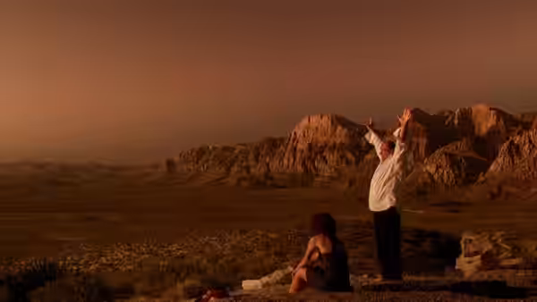 A man raises his arms beside a seated woman in a desert landscape