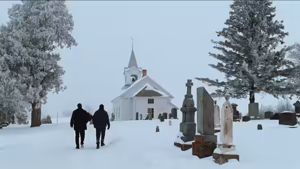 Two men walking through a snowy graveyard toward a white church