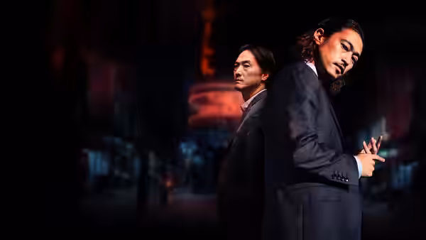 Two men in suits stand back to back on a neon-lit street at night