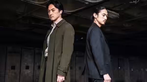 Two men stand facing forward inside a dimly lit concrete space