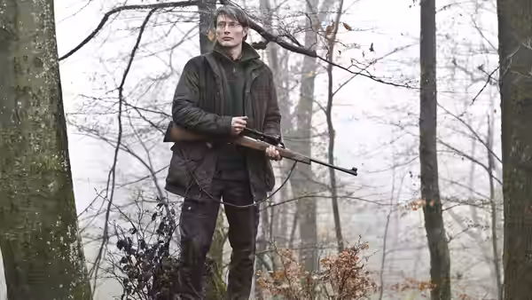 Lucas (Mads Mikkelsen) stands in misty woods holding a rifle