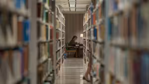 A woman seated at a desk in a long library aisle