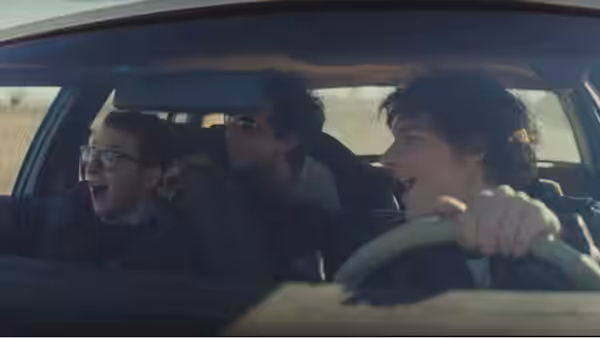 Three young men shout while riding inside a car through open countryside