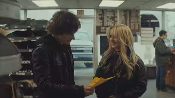 Young man in leather jacket hands a paper to a smiling blonde woman in a store